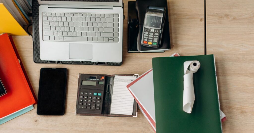 Bureau de micro-entrepreneur avec ordinateur portable, calculatrice, dossiers et terminal de paiement — préparation de la CFE 2026