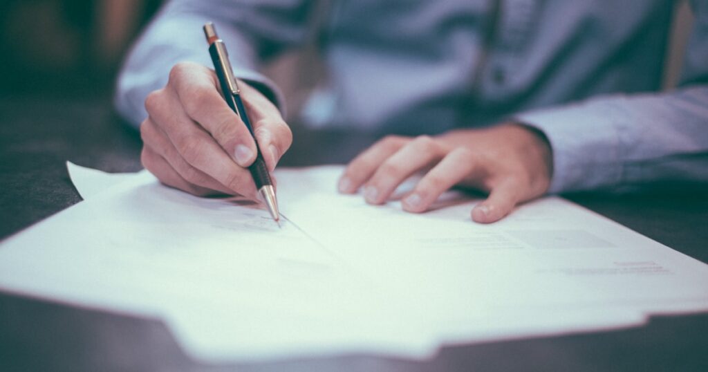 Personne remplissant des documents administratifs au crayon, illustrant la déclaration des cotisations sociales en micro-entreprise