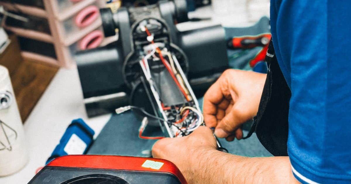 Mains d’un réparateur intervenant sur le câblage d’un aspirateur ouvert dans un atelier de réparation d’électroménager