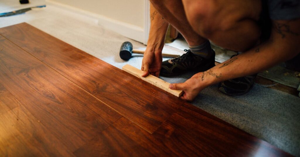 Mains d’un artisan posant des lames de parquet en bois avec une cale et un maillet, illustrant le métier de parqueteur