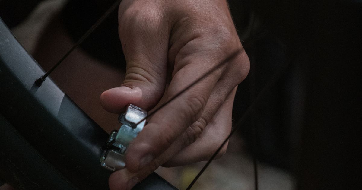 Main d’un réparateur réglant la tension des rayons d’une roue de vélo avec une clé à rayons