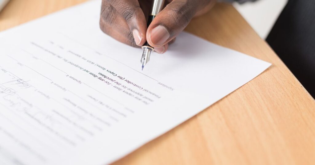 Main signant un contrat au stylo plume sur un bureau en bois